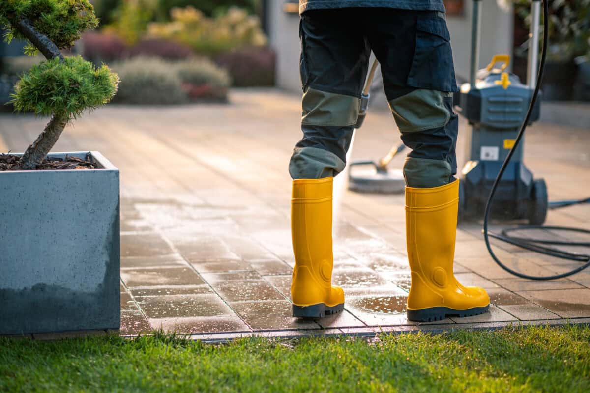 Cleaning a Patio With a Pressure Washer While Wearing Yellow Waterproof Boots in the Garden